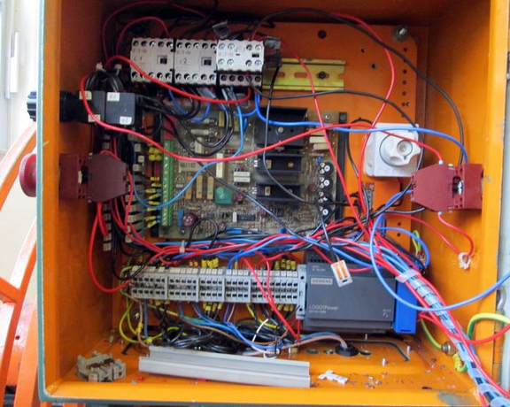 Geöffneter Schaltschrank mit Steuerplatine, Klemmen, Relais und zahlreichen verlegten Kabeln.