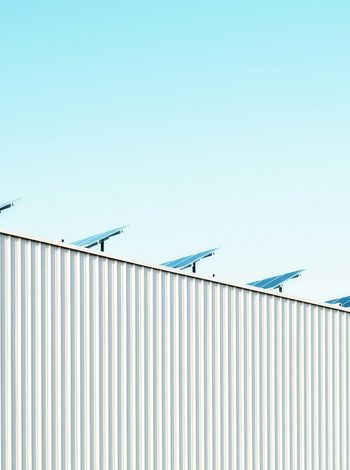 Solarpaneele auf der Dachkante eines Gebäudes mit heller Metallfassade vor blauem Himmel.