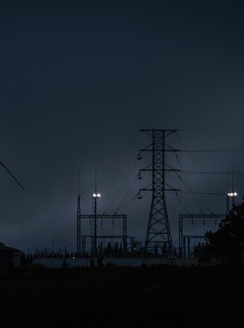 Windrad und Strommasten mit Umspannwerk bei Dunkelheit vor wolkigem Himmel.