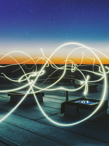 Lichtspuren über einem Flachdach bei Dämmerung symbolisieren Energiefluss und Strom.